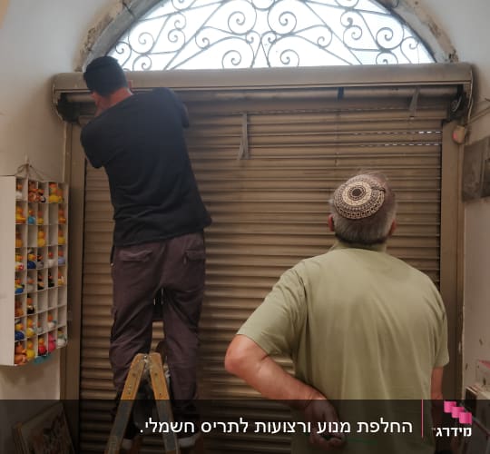 שני אנשים מתקנים תריס מתכת בחנות